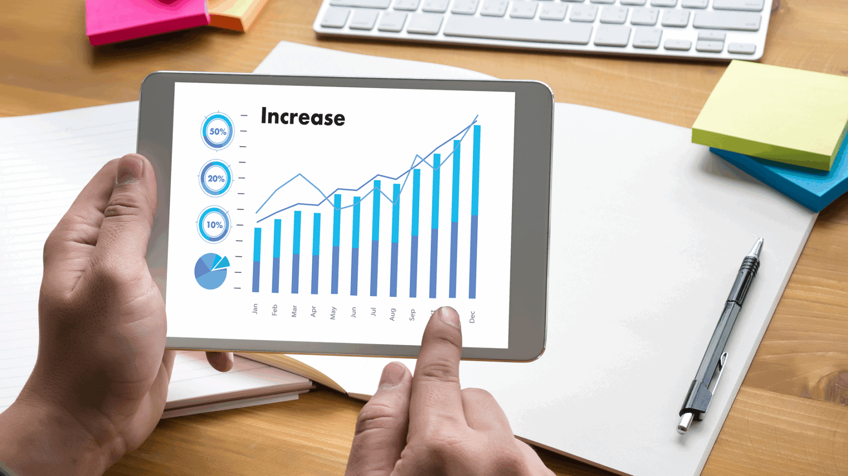 Person analyzing yearly business growth and performance increase using tablet with bar and line graph data visualization.