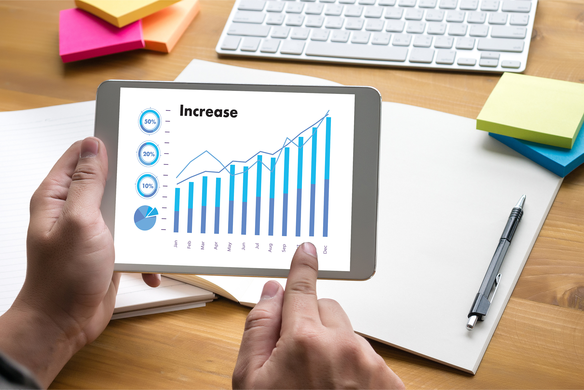 Person analyzing yearly business growth and performance increase using tablet with bar and line graph data visualization.